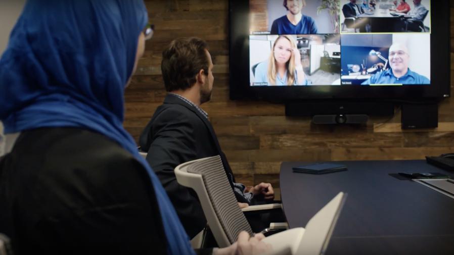 Personen an einem Konferenztisch bei einer Videokonferenz